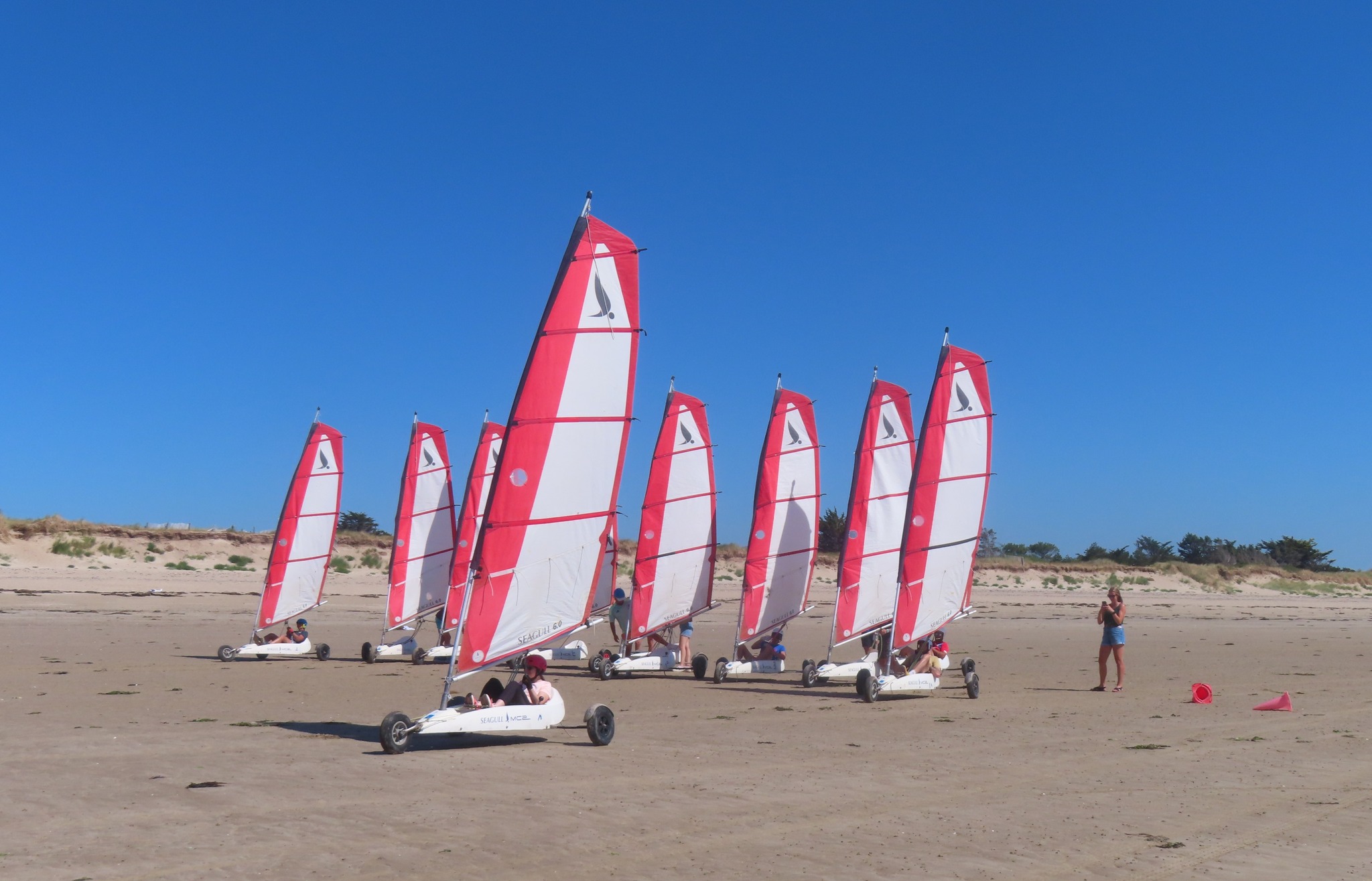 Des chars à voile aux voiles rouges sur la plage sous un grand ciel bleu